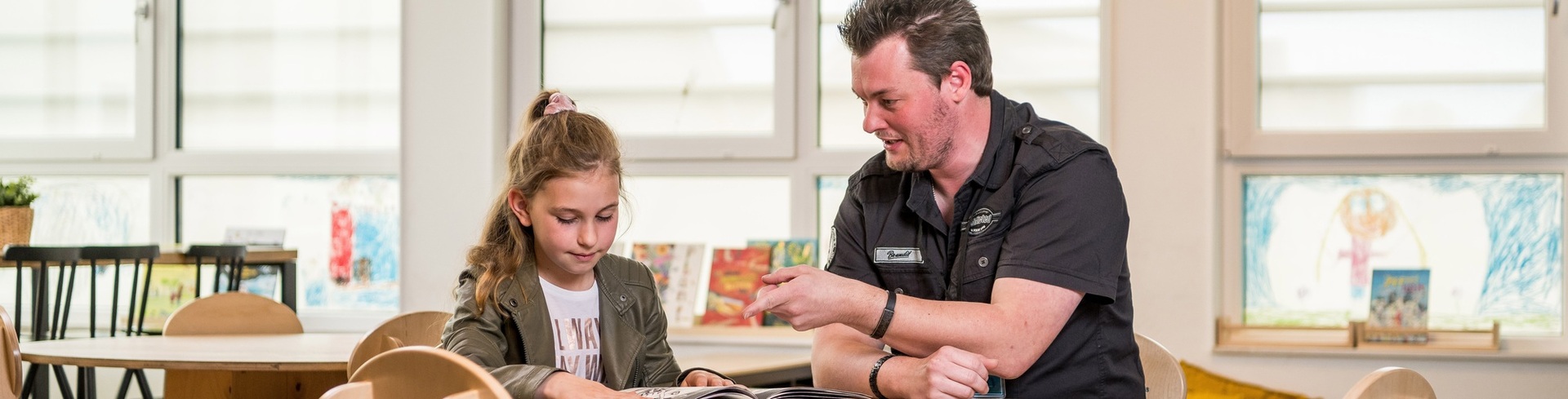 "leerwerkburo reintegratie man in zwart overhemd aan tafel met een meisje op een basisschool"